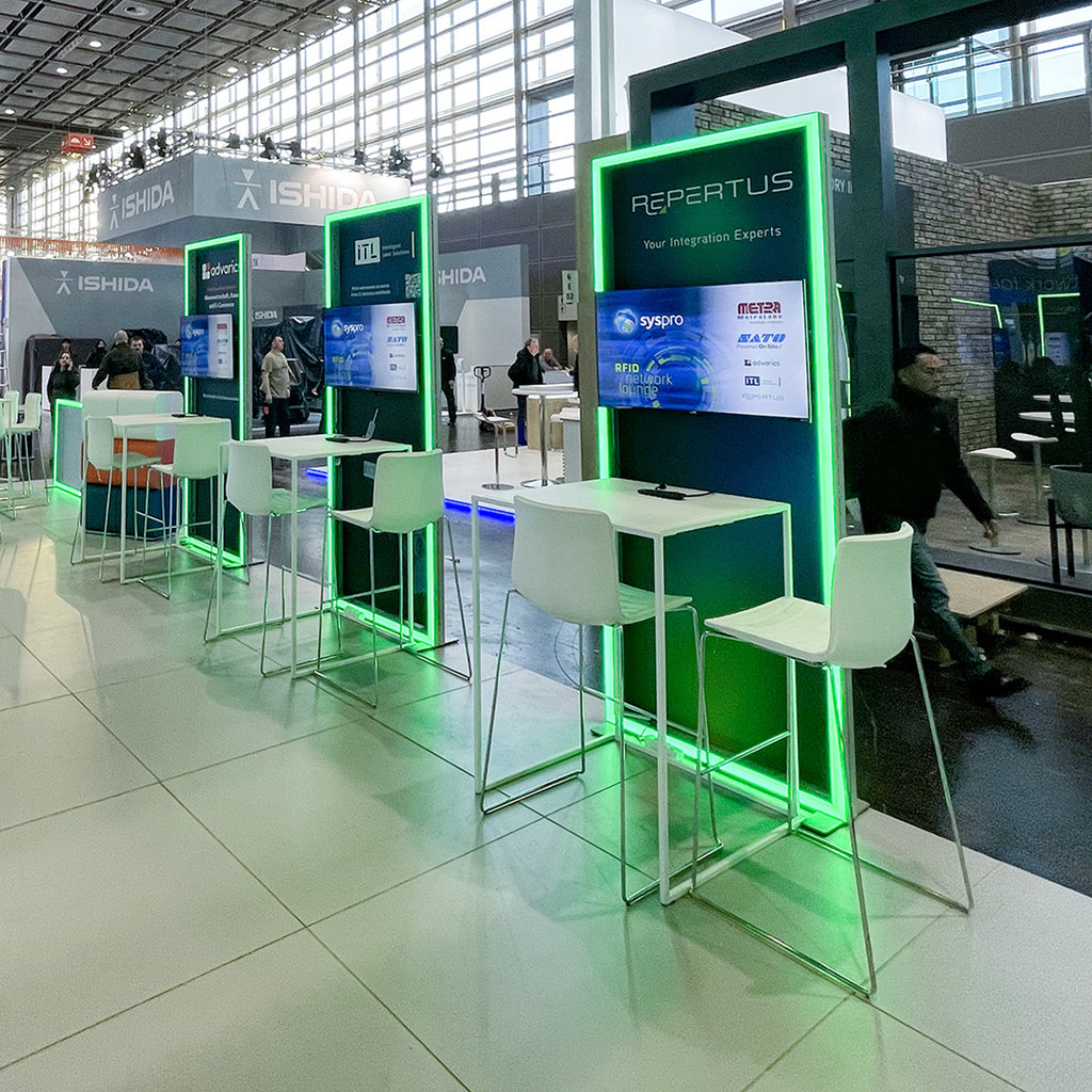 Messestand von Repertus mit grünen LED-Leuchtkonturen von Modulap. Der Stand bietet moderne Präsentationsflächen mit Displays und Sitzbereichen, die eine einladende Umgebung für Gespräche und Produktpräsentationen schaffen.