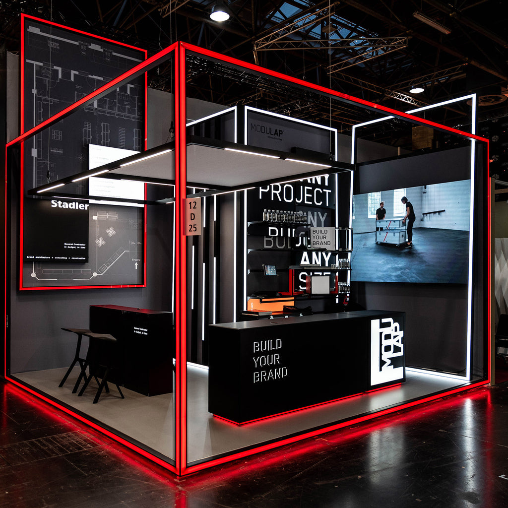 Messestand von Modulap mit markanter LED-Leuchtkontur in Rot und Weiß. Der Stand präsentiert modernste Designlösungen für Markenauftritte mit interaktiven Displays, stilvollen Möbeln und einer futuristischen Struktur, die die Botschaft 'Build Your Brand' hervorhebt.