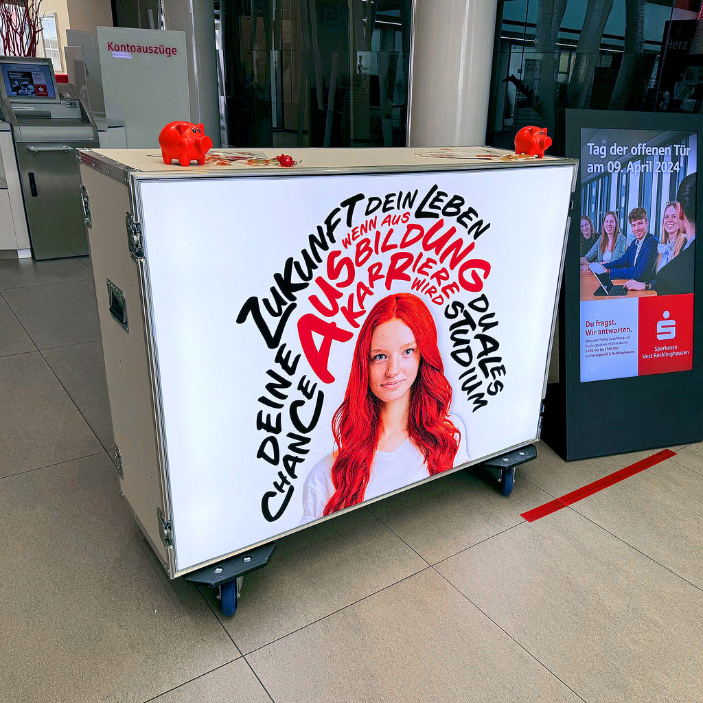 Flightcase Counter von Modulap im Sparkassen-Design, beleuchtet mit einer Werbebotschaft zu dualer Ausbildung und Studium. Der Counter zeigt eine junge Frau umgeben von markanten Schriftzügen, die auf Karrierechancen aufmerksam machen.
