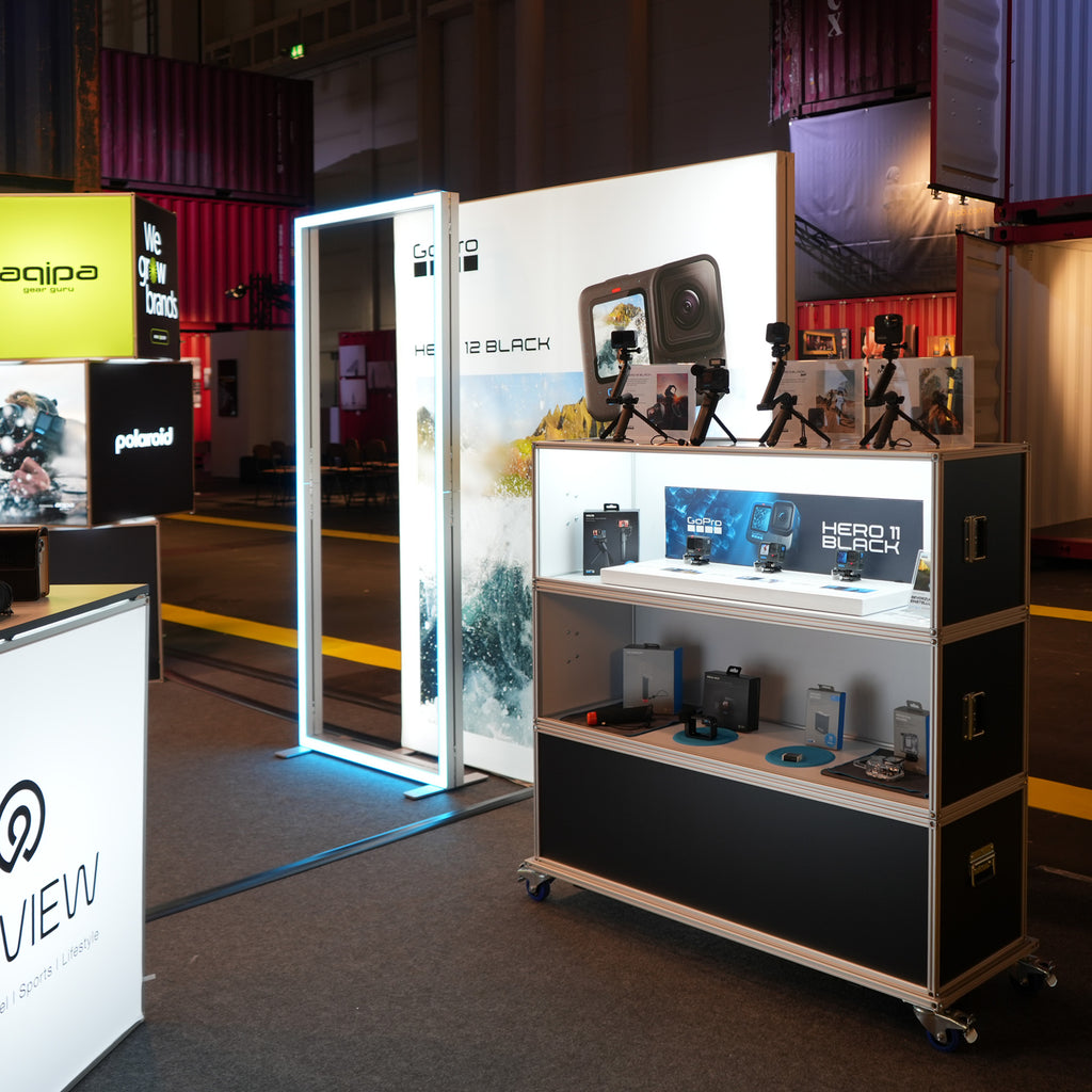 Polaroid Messestand mit beleuchtetem Display und Modulap Cases, die GoPro HERO 11 Black und HERO 12 Black Kameras präsentieren. Der Stand nutzt moderne LED-Leuchtrahmen und modulare Vitrinen von Modulap für eine stilvolle und ansprechende Produktpräsentation.