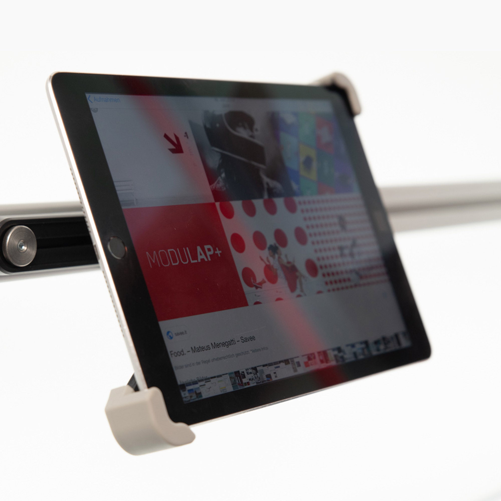 Ein iPad, das in einem modernen Halter befestigt ist, zeigt die Benutzeroberfläche mit dem Logo 'MODULAP+'. Der Halter ist an einer horizontalen Stange montiert und bietet eine stabile und flexible Präsentationslösung. Ideal für Messen oder Ausstellungen, um digitale Inhalte interaktiv darzustellen. Der Hintergrund ist minimalistisch und lenkt die Aufmerksamkeit auf das iPad und den Halter.