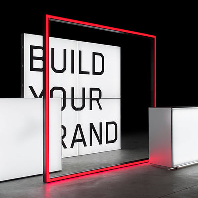 Modularer Messestand mit beleuchtetem Schriftzug 'Build Your Brand' – Stilvolles Design mit leuchtendem roten Rahmen und weißem Counter für markenorientierte Präsentationen.