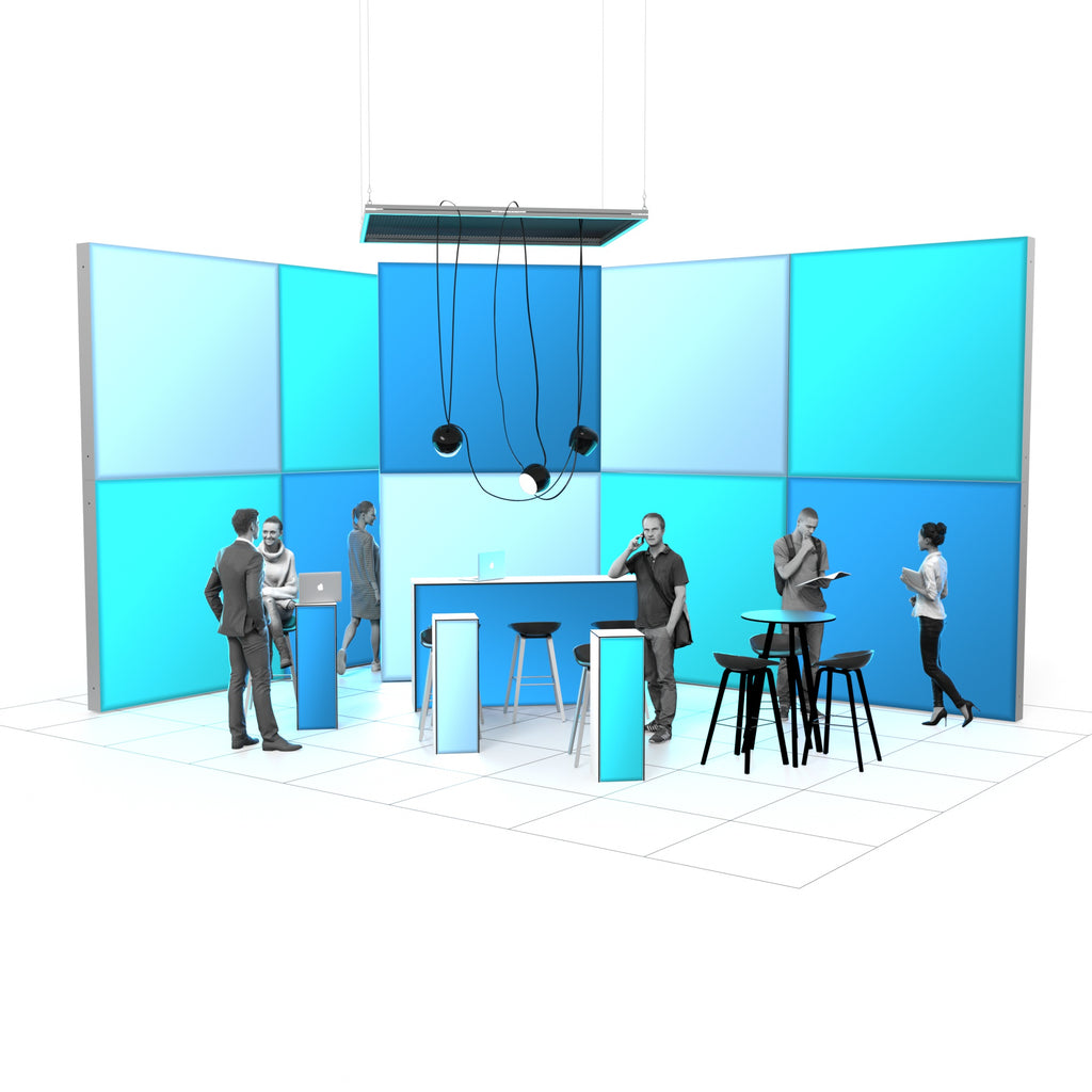 Der Messestand ist offen und modern mit großen blauen Wandpaneelen gestaltet. In der Mitte befindet sich ein Tresen mit Barhockern, darüber hängen mehrere Lampen an einer abgehängten Leuchtkontur. Mehrere Personen stehen im Raum, führen Gespräche, arbeiten am Laptop oder lesen Unterlagen. Rechts gibt es einen Stehtisch mit Hockern.