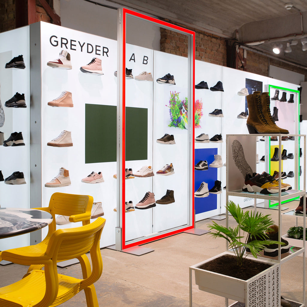 Messestand von Greyder mit LED-Lightboxen von Modulap und Lightframes, die verschiedene Schuhmodelle präsentieren. Die Schuhe werden mit Magnethaltern an den Lightboxen befestigt, während farbige Akzentränder und grüne Pflanzen dem Stand ein modernes und frisches Design verleihen.