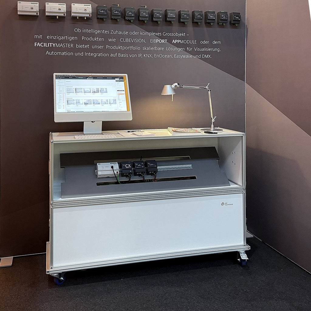 Messestand mit Modulap Case, das als Präsentationsstation für intelligente Haus- und Gebäudeautomation dient. Der Stand zeigt ein Display mit Software-Demonstration, Steuergeräte und eine stilvolle Tischleuchte. Modulap Case kombiniert Funktionalität und Design, ideal für Produktpräsentationen auf Messen.