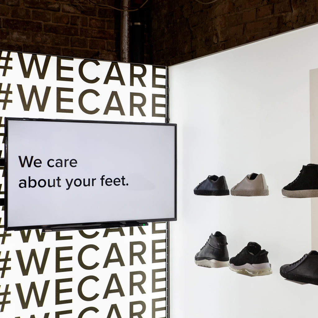 Modulap-Messestand mit modernem Schuhdisplay und leuchtender Rückwand mit #WECARE Schriftzug. Highlight: Monitor zeigt den Text 'We care about your feet', betont die Markenbotschaft und Produktpräsentation.