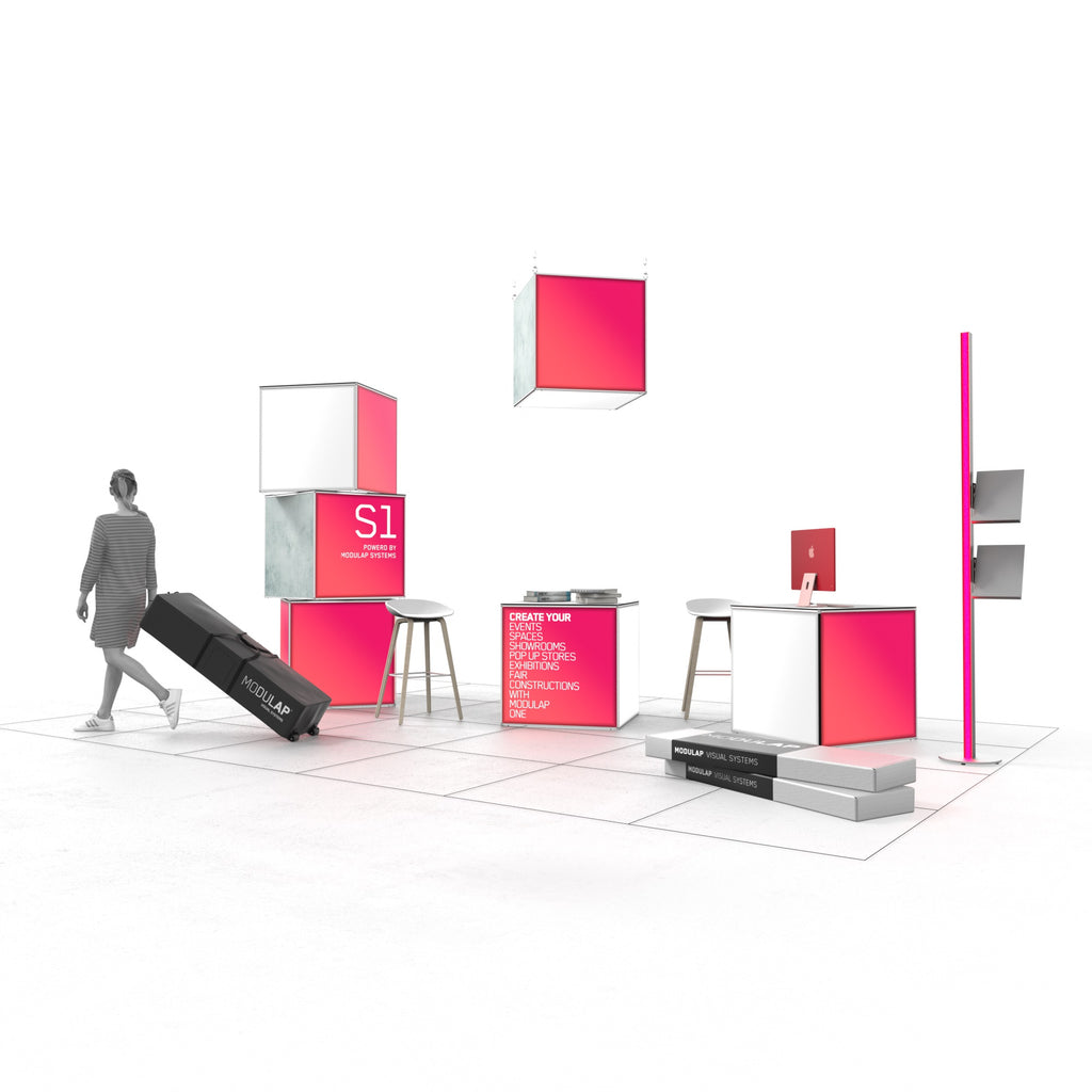 Der moderne Messestand von Modulap ist mit auffälligen LED-Leuchtwürfeln in Pink und Weiß gestaltet. Ein großer pinkfarbener Würfel thront auf einem grauen Würfel, während ein weiterer pinkfarbener Würfel von der Decke hängt. Ein Counter mit Stühlen und ein zusätzlicher Tisch bieten Präsentationsflächen. Eine Frau zieht einen Modulap-Rollkoffer vorbei. Die gesamte Szenerie schafft eine stilvolle und einladende Präsentationsumgebung.