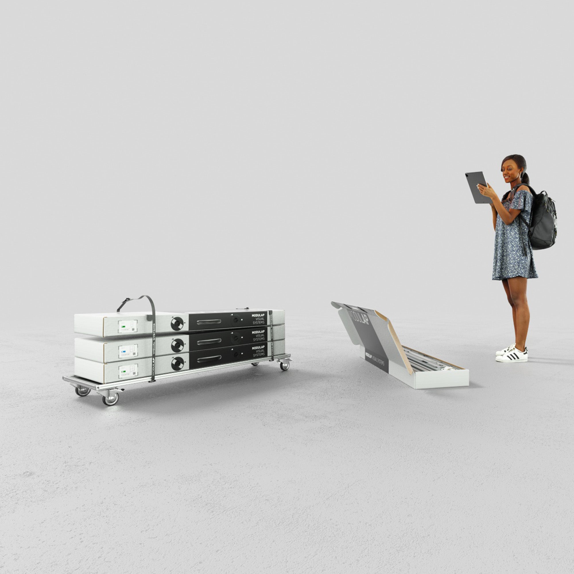 Das Bild zeigt eine Verpackungslösung für einen Promotionstand von Modulap. Links sind Modulap-Elemente auf einem Rollbrett gestapelt, rechts sind weitere Komponenten in einer Systemverpackung organisiert. Eine Frau mit einem Tablet steht lächelnd daneben.